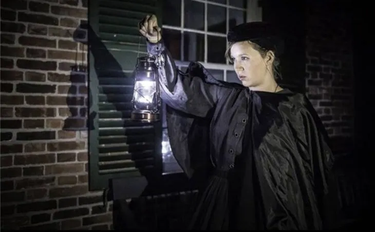 A guide in period dress holding a lantern on a Haunted History tour.
