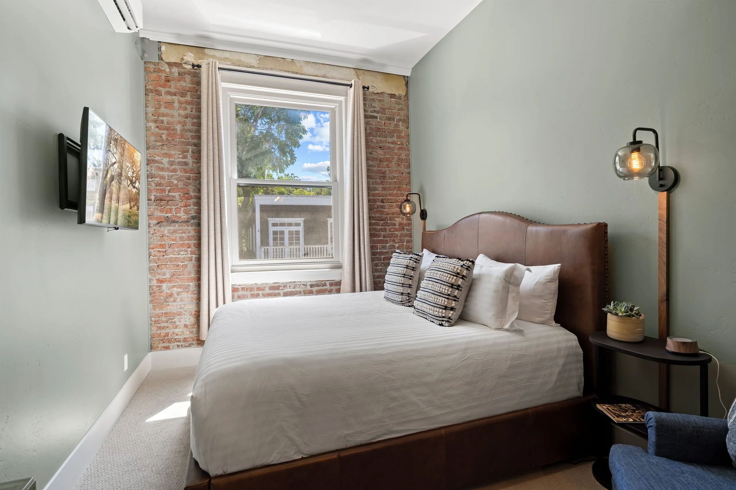 Room #6 at the Jacksonville Inn: Soft sage walls, a leather headboard and a blue armchair by the window.